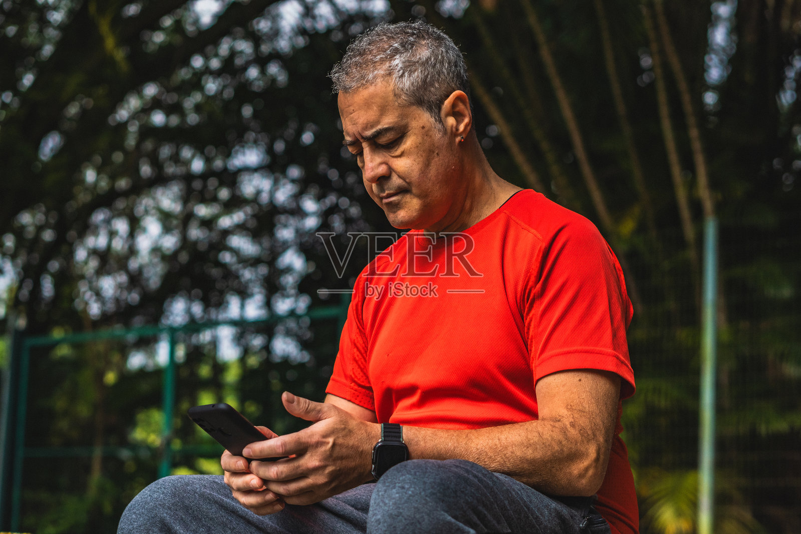 中年白人男性在巴西圣保罗的公园里，在阳光明媚的日子里查看他的智能手机信息照片摄影图片