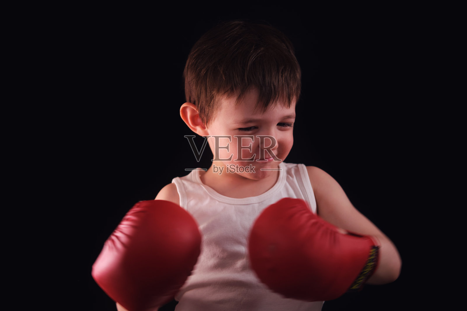 一个决心坚定的年轻人，穿着拳击服，正在为一场重要的比赛进行心理准备。这位穿着红色手套的小运动员展现了真正战士的心态。三岁的小孩。照片摄影图片