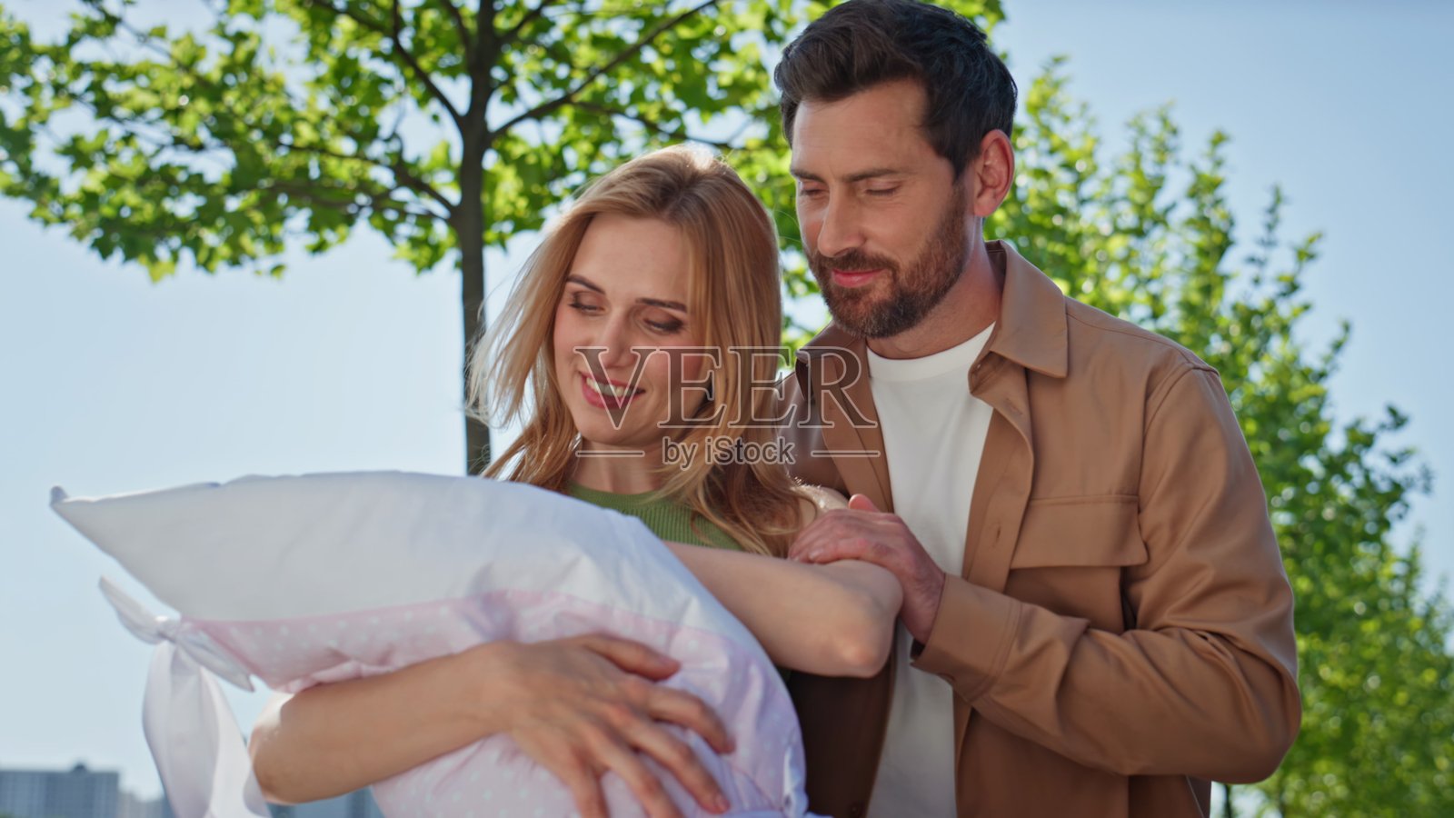 父母在绿意盎然的地方近距离欣赏新生儿，温馨相拥。照片摄影图片