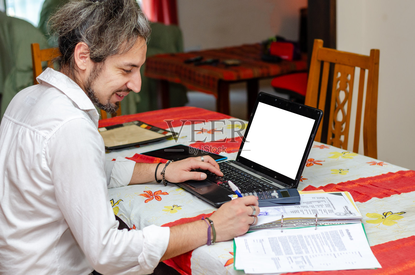 微笑的男子在家中使用笔记本电脑和计算器，正在纸上写字照片摄影图片