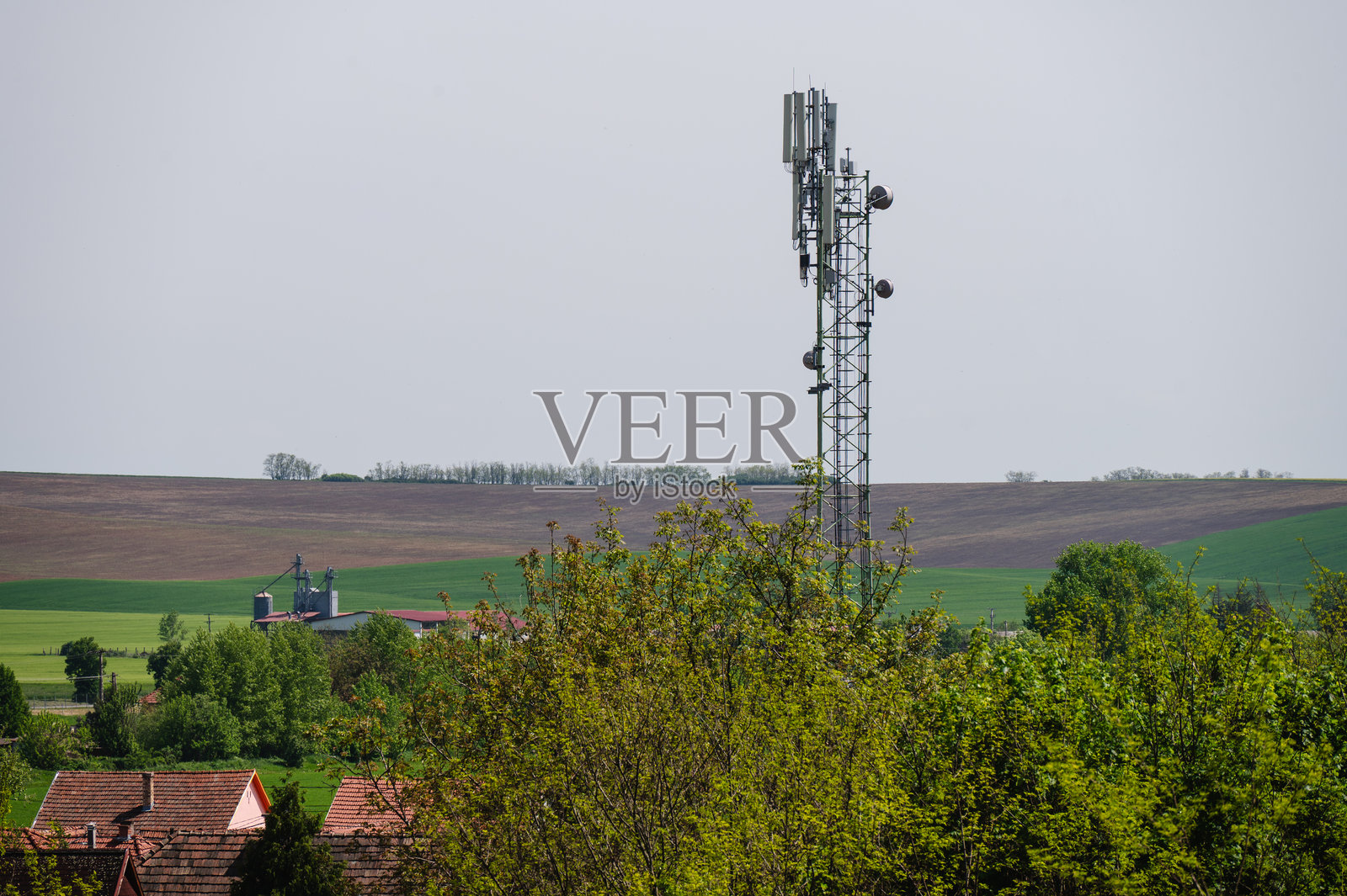乡村风景中的信号塔，周围是田野和屋顶照片摄影图片