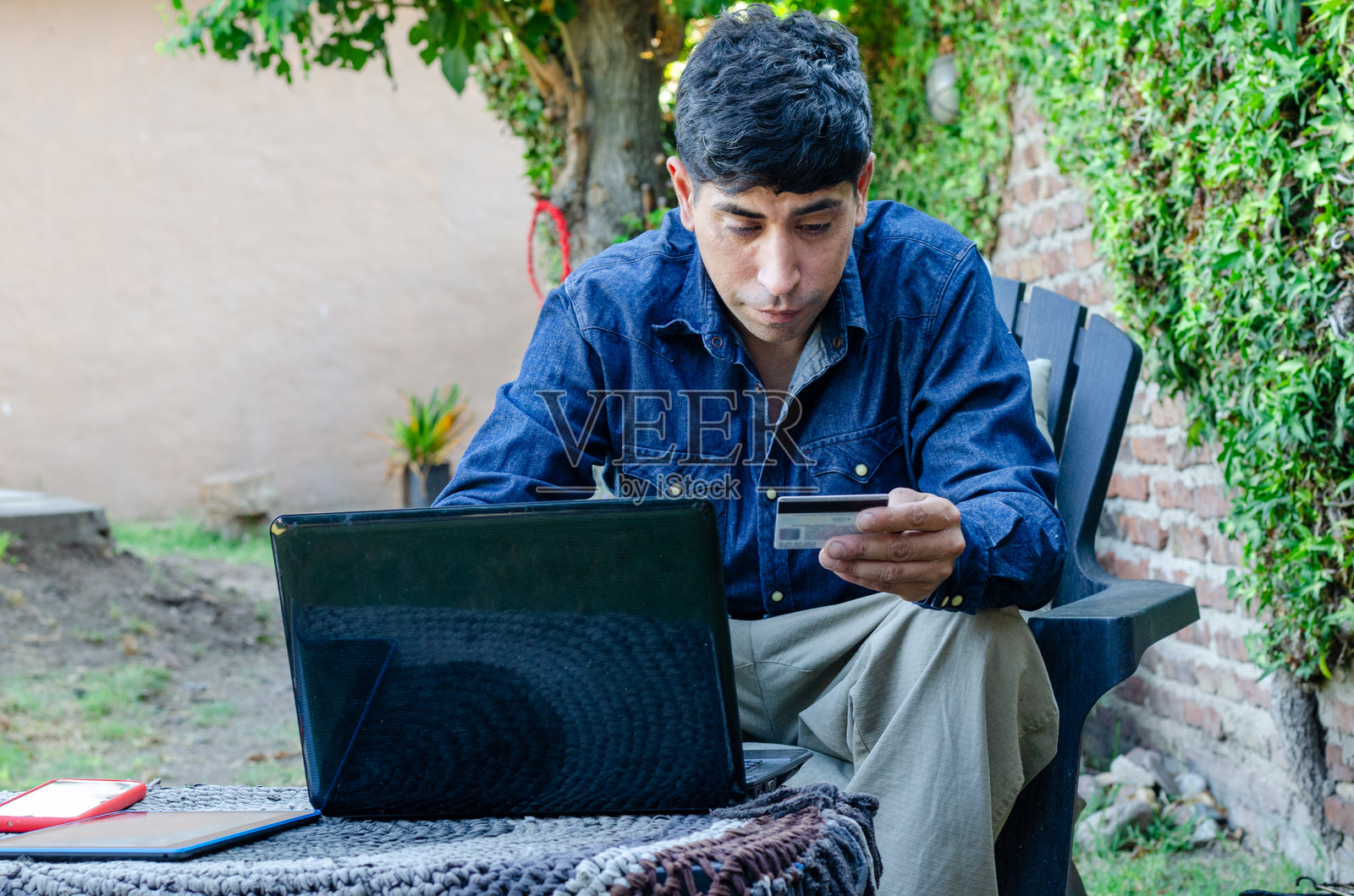 男子在户外使用信用卡，旁边有笔记本电脑、手机和数码平板。照片摄影图片