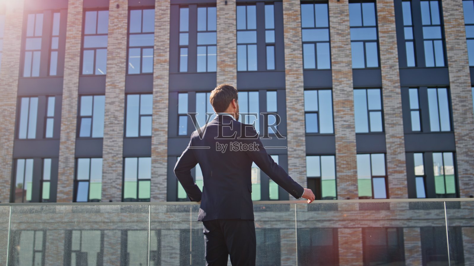 商人从背后观看阳光明媚城市的建筑，企业家站立着。照片摄影图片