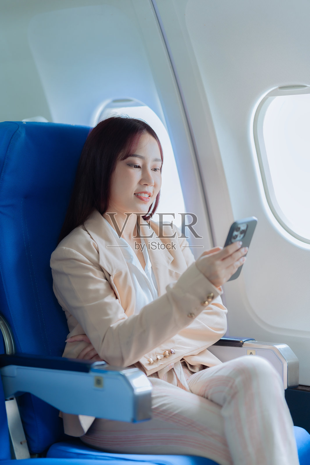 亚洲女性在飞机上坐在窗边，手持智能手机，正在阅读社交网络新闻或使用旅行应用程序。照片摄影图片