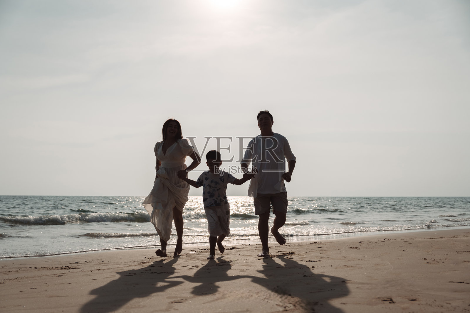 快乐的亚洲家庭在海滩度假时一起享受。家庭成员手牵手，享受海边的日落。快乐的家庭旅行，周末家庭假期。照片摄影图片