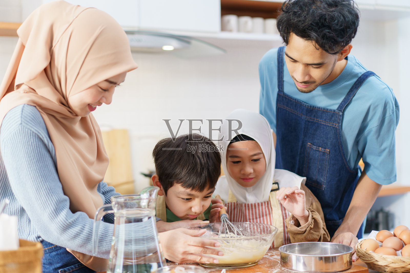 亚洲穆斯林女性和可爱的孩子们正在厨房里准备和烹饪。照片摄影图片