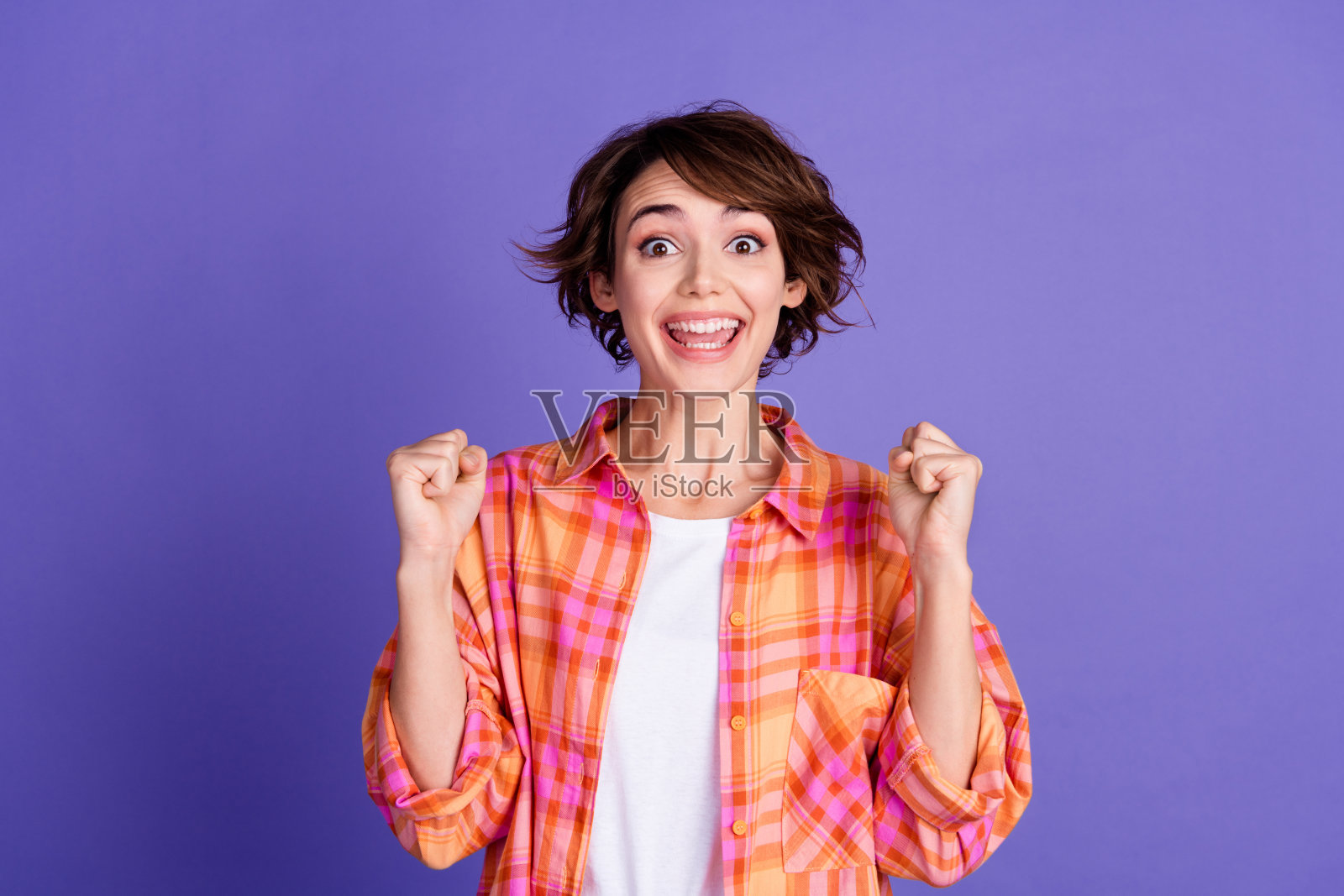 年轻女士的肖像，举起拳头，穿着衬衫，背景为紫色。照片摄影图片