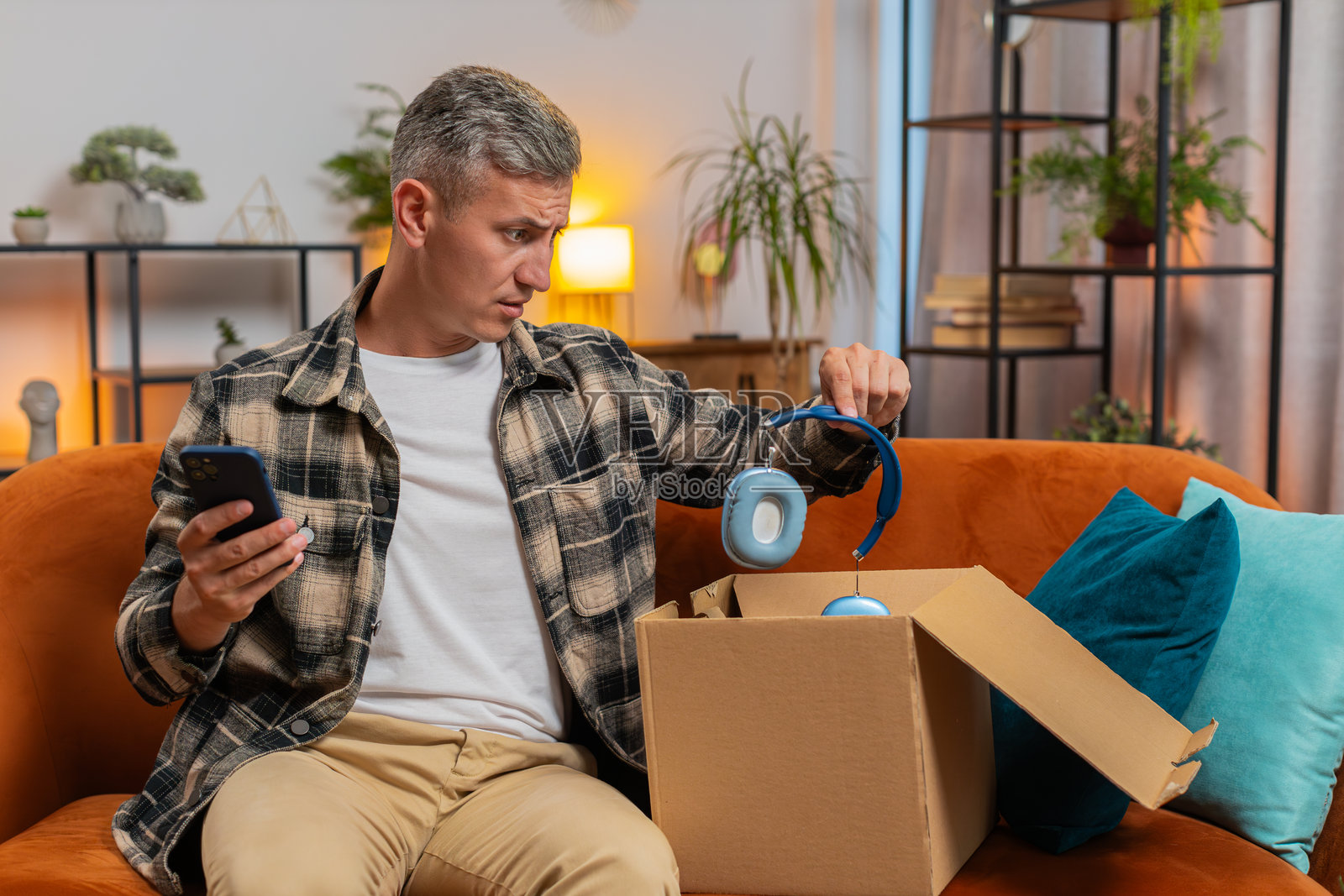 不快乐的男人在拆箱，感到对收到的损坏无线耳机不满意。照片摄影图片