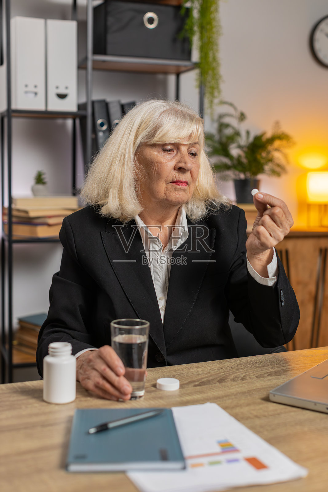 生病的老年女商人头痛，正在家中服药并使用笔记本电脑工作照片摄影图片