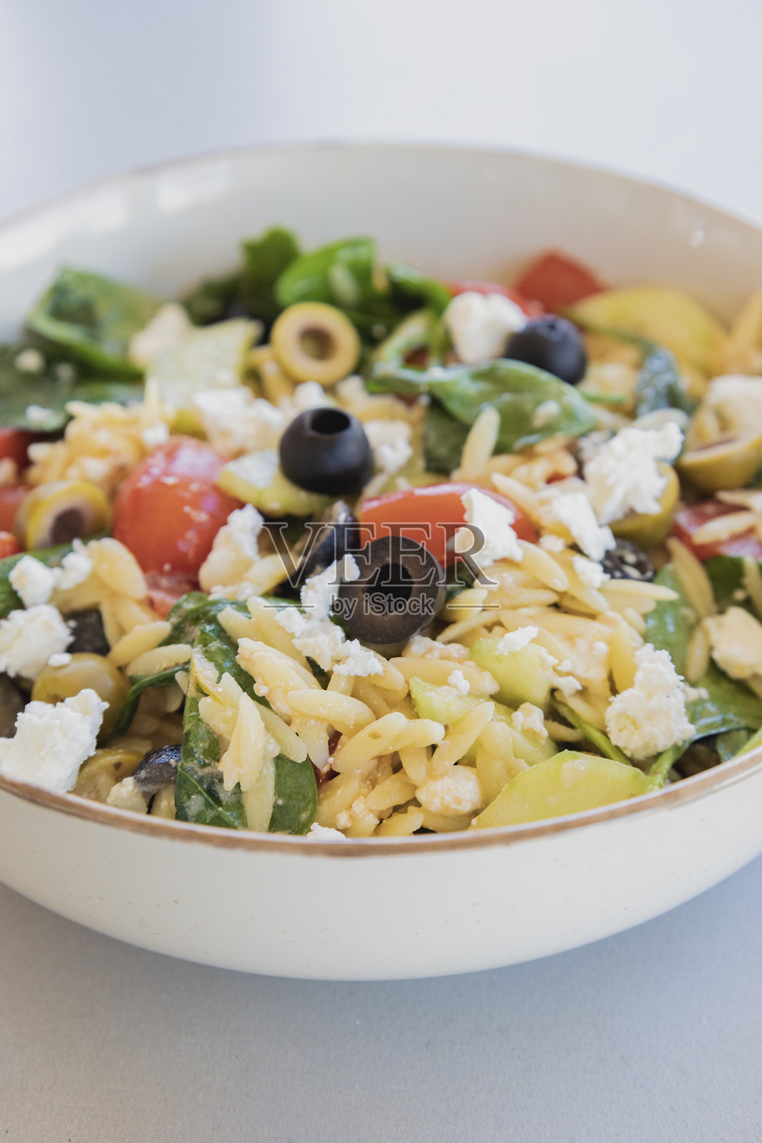 新鲜蔬菜、黑橄榄和碎羊奶酪制成的健康意大利米沙拉，盛在碗中，特写镜头。照片摄影图片