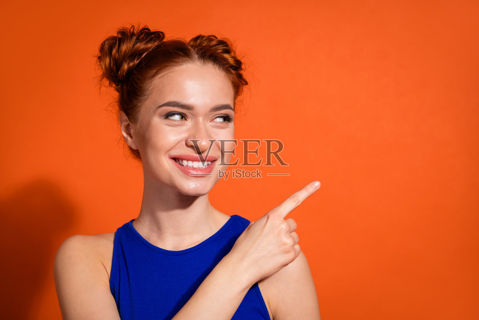 穿着蓝色上衣的年轻女性在橙色背景前微笑并用手势表达。照片摄影图片