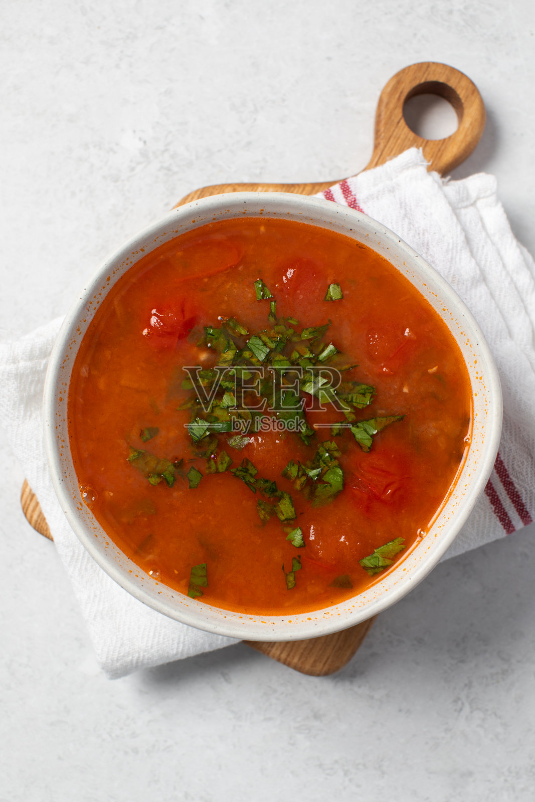 白色碗中的新鲜蔬菜汤，配有番茄和香草，放在亚麻餐巾上。照片摄影图片