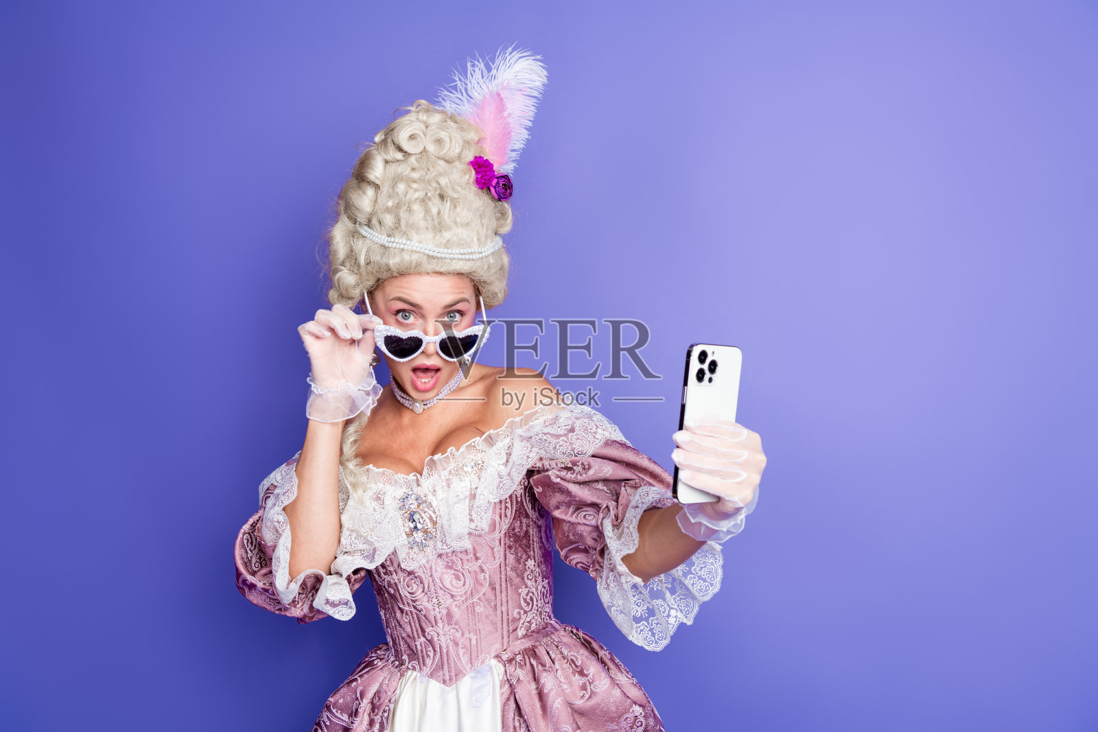 身穿历史服装的优雅女性在紫色背景前摆姿势，手持现代智能手机照片摄影图片