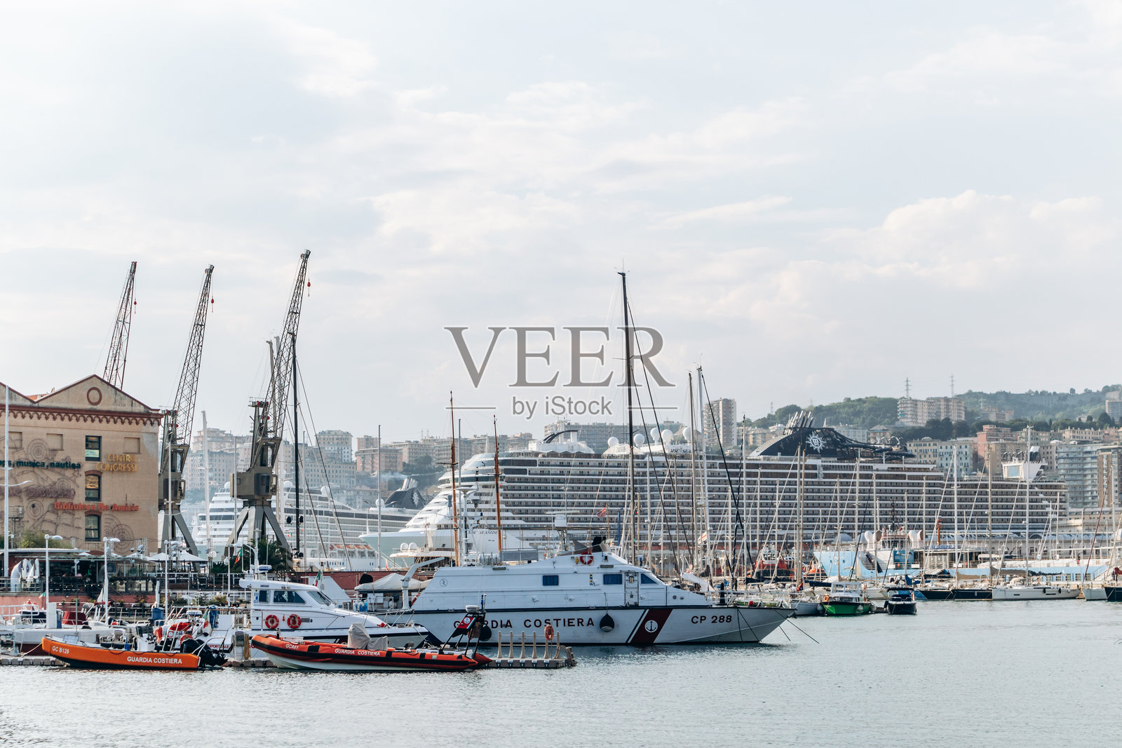 海岸警卫队船只、帆船和一艘大型游轮停靠在繁忙的港口，背景是城市天际线。照片摄影图片