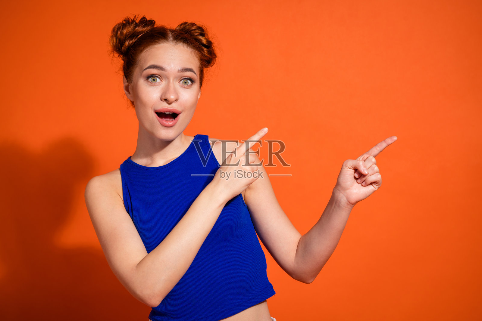 充满活力的年轻女性在鲜艳的橙色背景下用手指兴奋地做出手势照片摄影图片