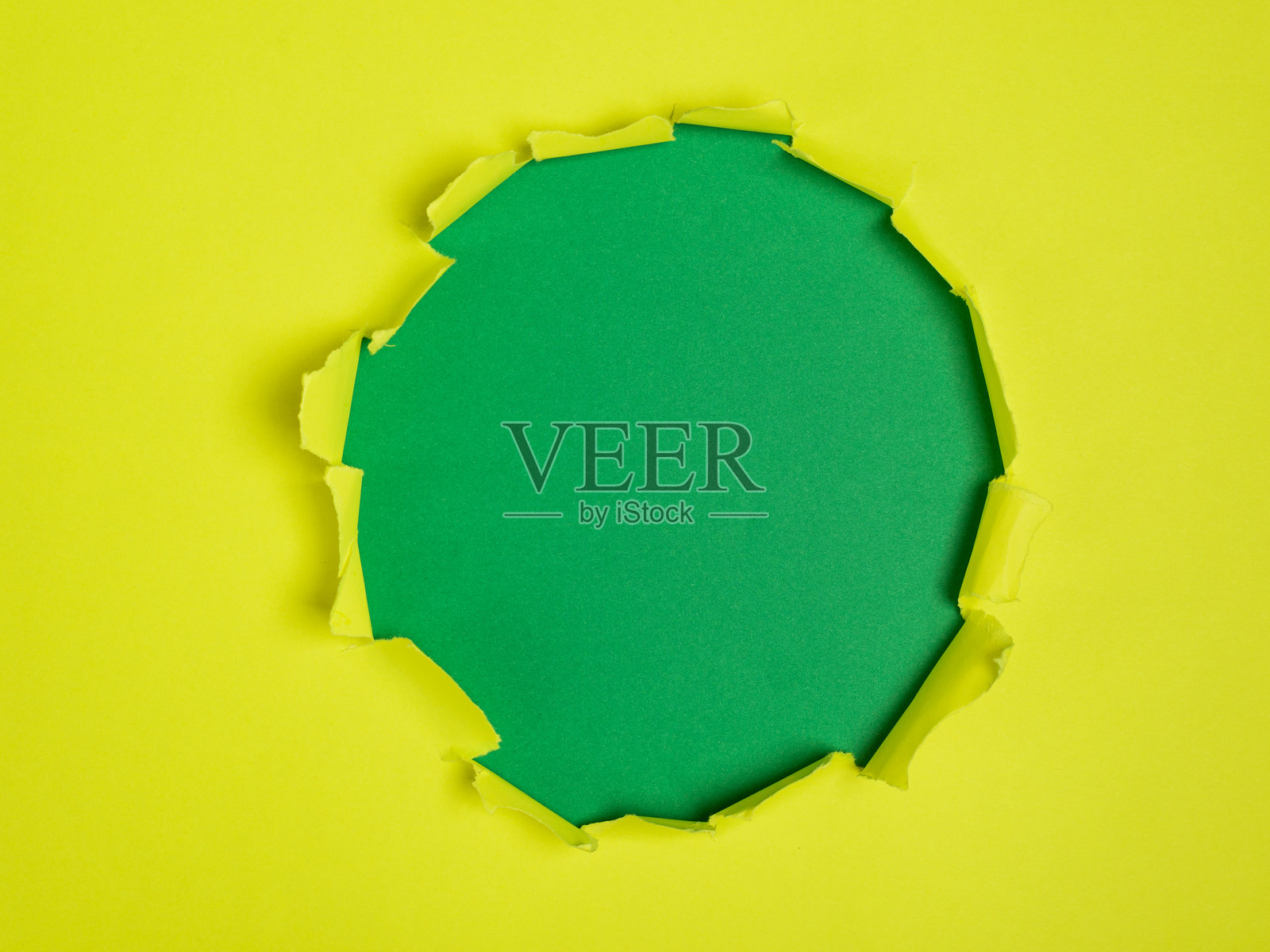 一张黄色纸张上有一个粗糙撕开的圆形开口，露出了一个纯绿色的背景。照片摄影图片
