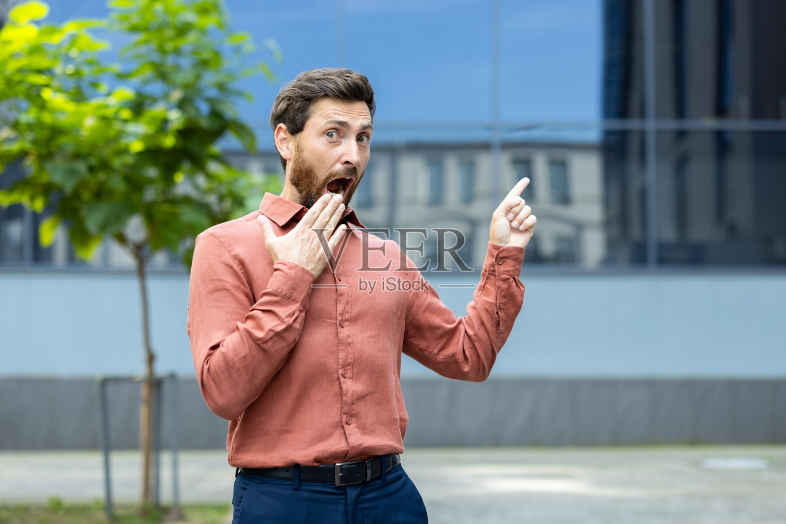 惊讶的男人张嘴指向天空，仿佛刚刚在城市中目睹了令人难以置信的事情。照片摄影图片