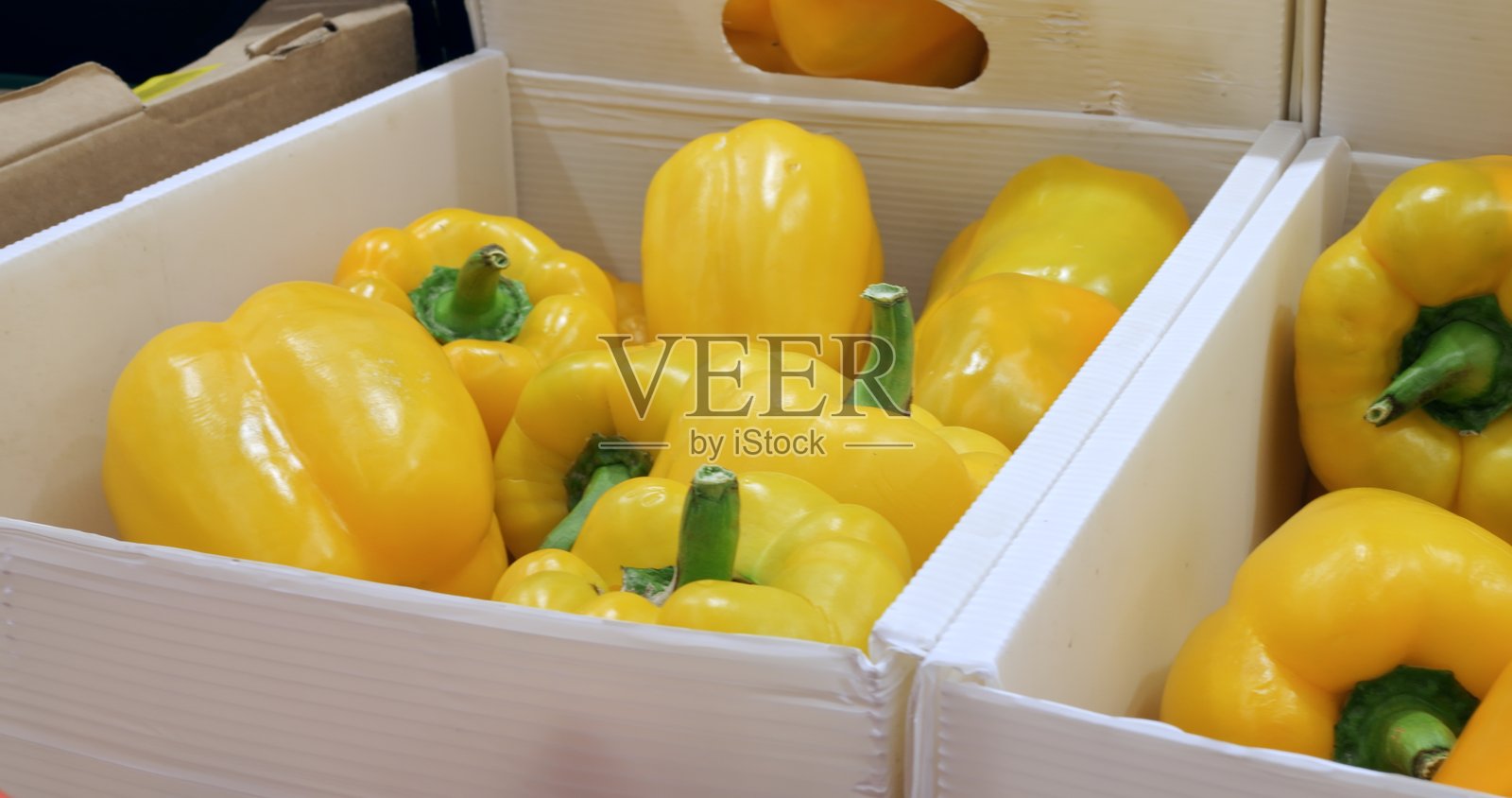 多个装满成熟黄色甜椒的白色纸箱整齐地排列在一起，形成了一个吸引人的展示，准备在杂货店出售。 有机蔬菜的概念。照片摄影图片