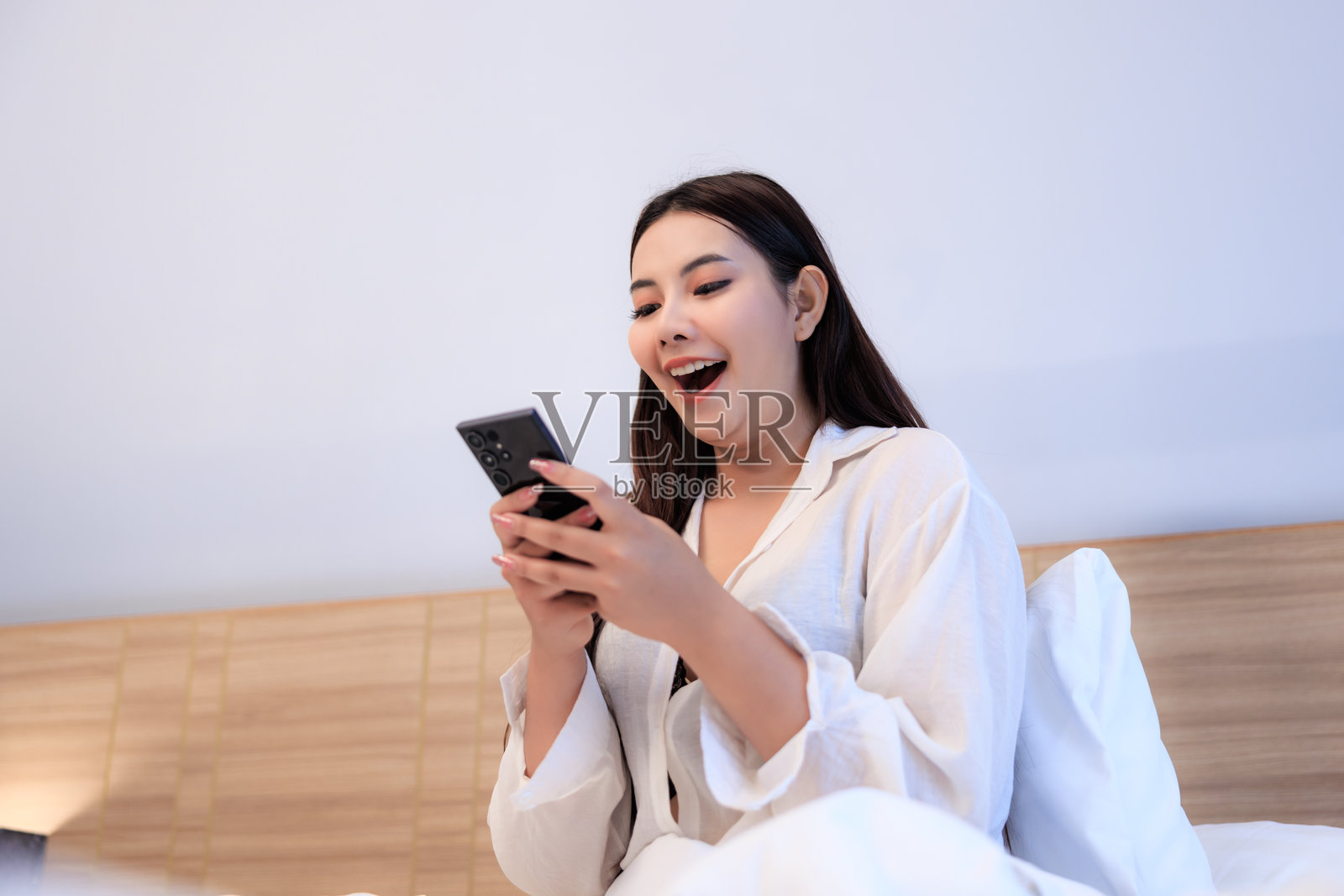 亚洲女性坐在床上愉快地使用智能手机照片摄影图片