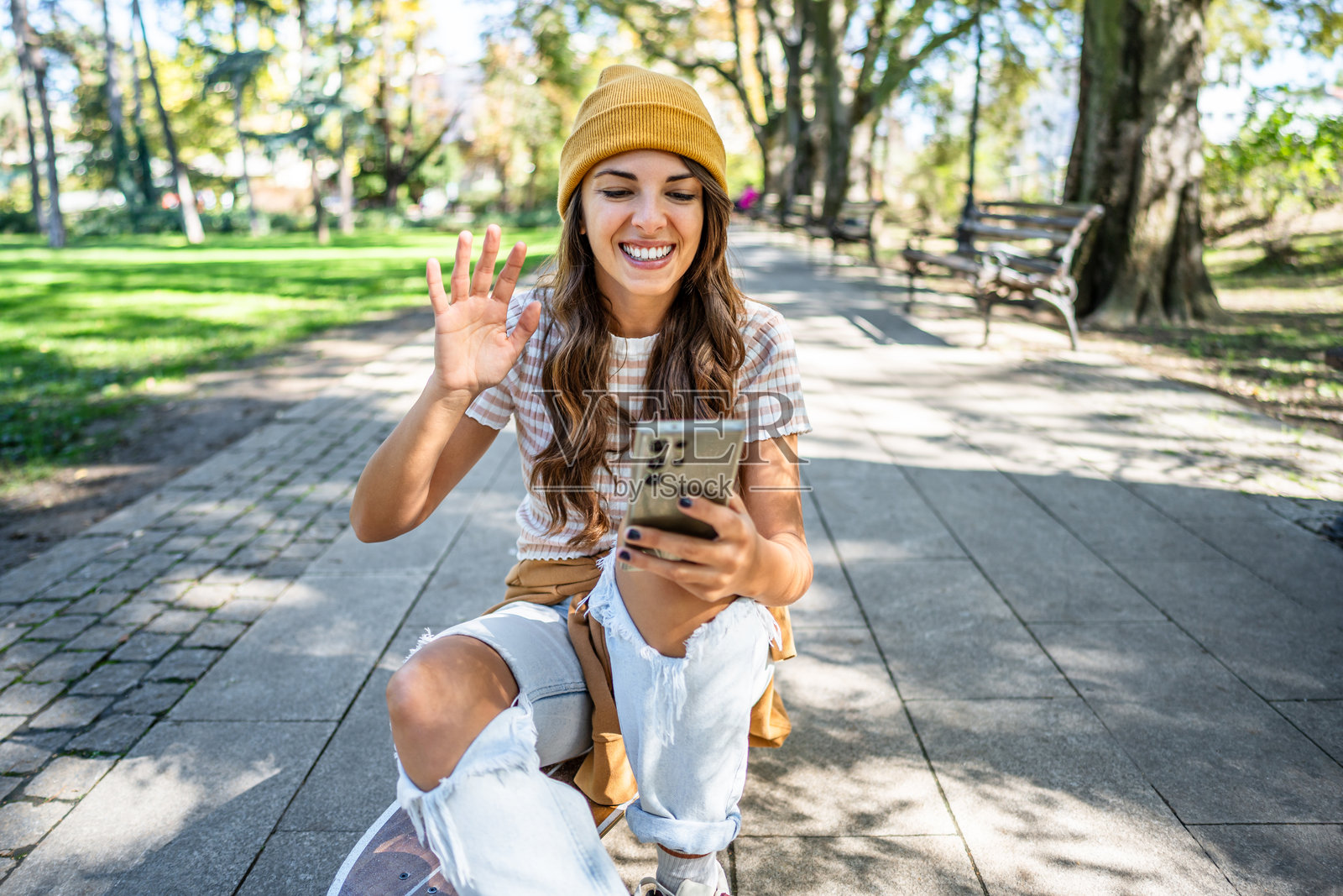 年轻女性在公园里坐在滑板上视频通话照片摄影图片
