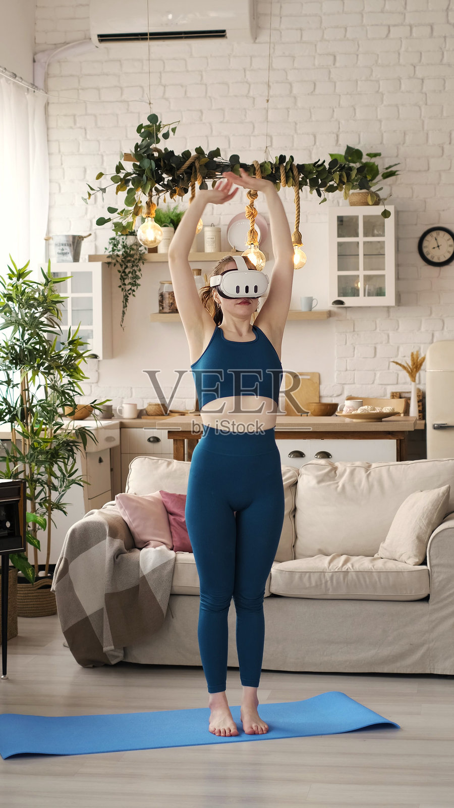 一位女性在时尚的客厅里单脚站立，佩戴着虚拟现实头盔进行平衡练习。这个场景强调了健身与尖端虚拟现实技术的融合。照片摄影图片