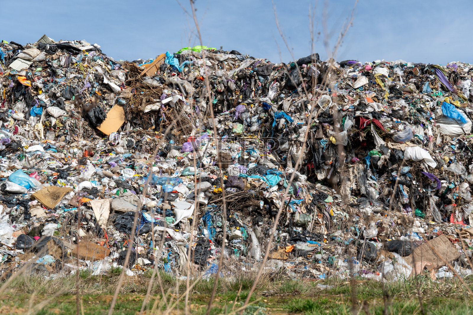 一大堆各种废弃物在明亮的天空下高耸，突显了废物积累的规模及其对环境的影响。照片摄影图片
