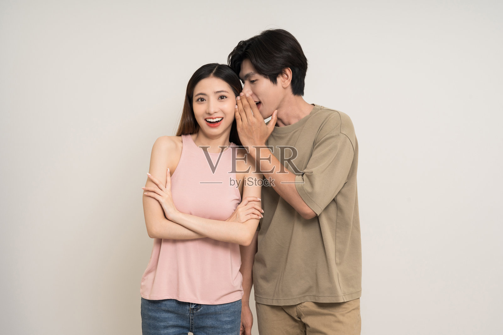 低声说着秘密八卦的快乐亚洲情侣，吸引人的各种动作姿势，站在孤立的白色背景上。愉快微笑的年轻男女在低声交流一些秘密八卦。照片摄影图片