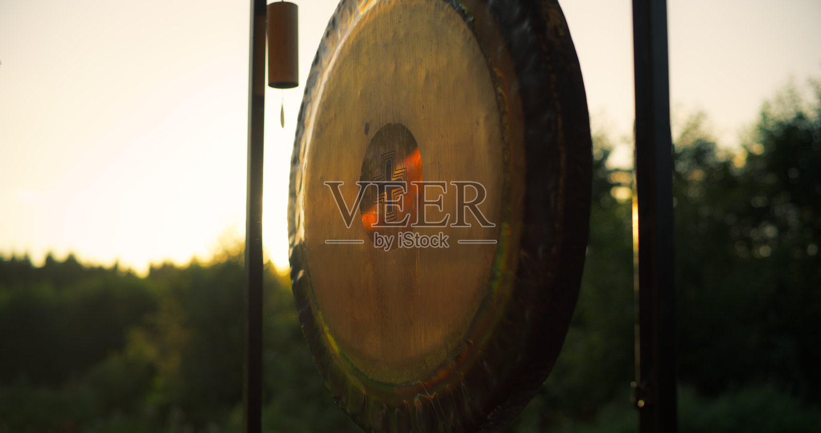 在日落的金色光辉中悬挂，锣声在空气中回荡。深沉的震动引导着瑜伽静修中心的冥想练习。照片摄影图片