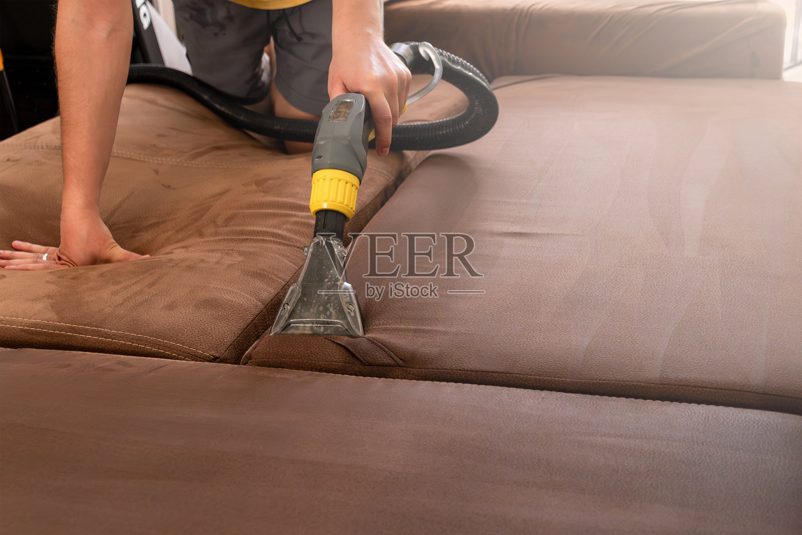 用洗尘吸尘器清洁棕色沙发。公寓里的春季大扫除照片摄影图片