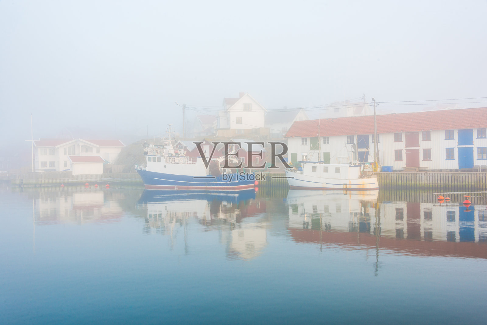 瑞典克拉德斯霍尔门的雾气港口，渔船和五彩斑斓的房屋倒映在宁静的水面上照片摄影图片