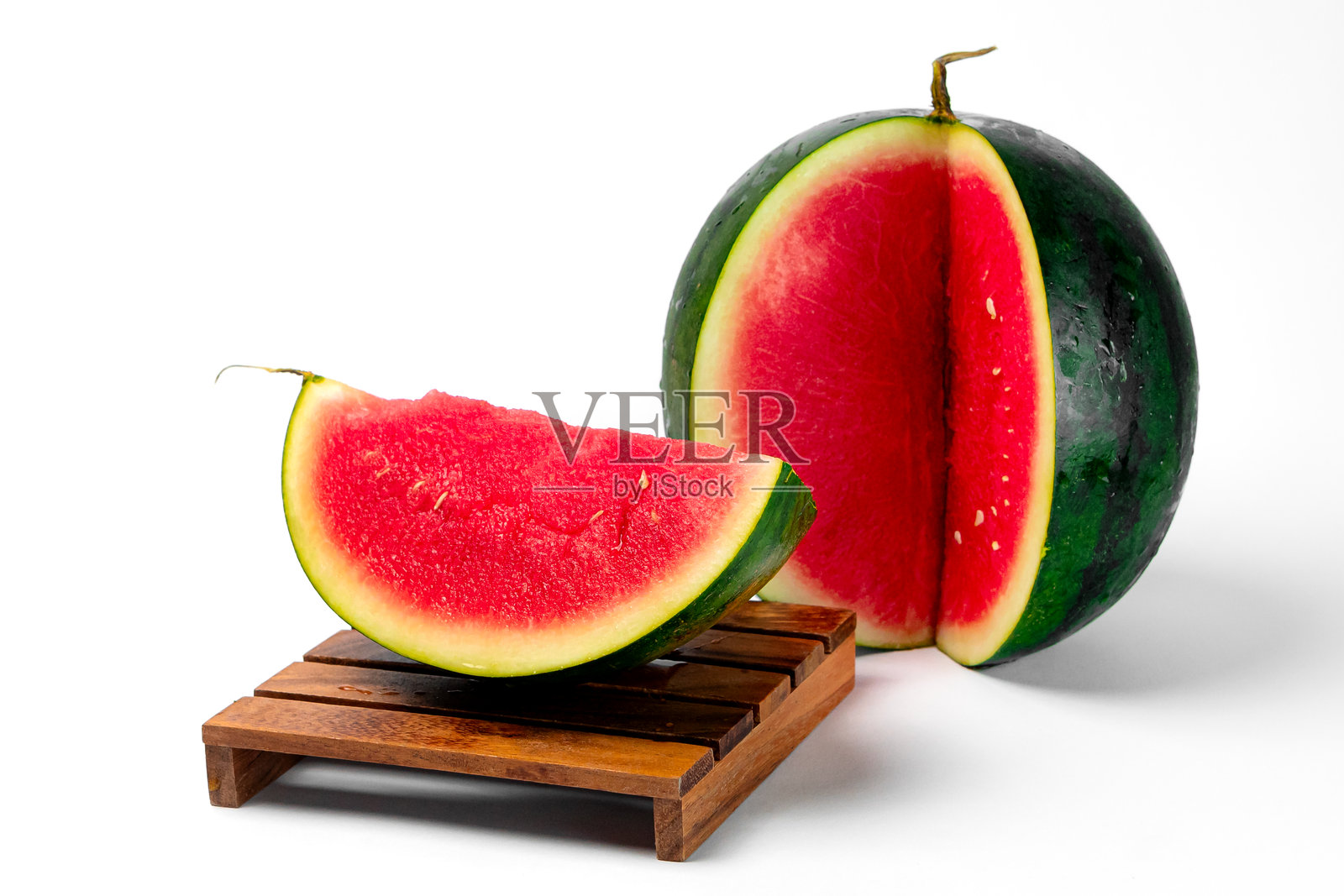 新鲜成熟的西瓜切成两半，旁边放着一片切好的西瓜，放在木托盘上，背景为白色。多汁的红色果肉和绿色的外皮，完美适合夏季消暑。照片摄影图片