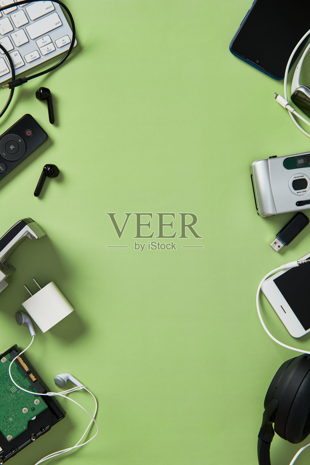 各种电子设备的平铺图，包括键盘、手机、耳机，背景为绿色。电子废物、科技杂乱或回收的概念。留白空间。照片摄影图片