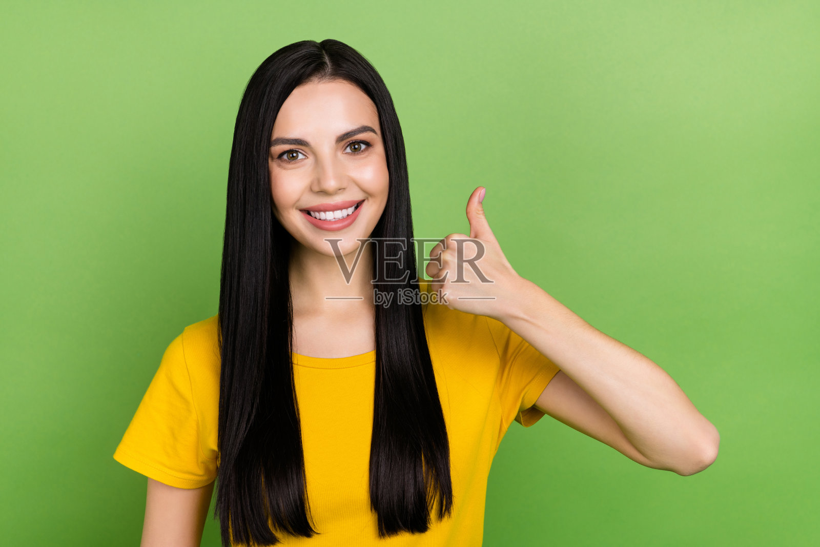 迷人积极的女孩露出灿烂的微笑，竖起大拇指，面向镜头，背景为绿色。照片摄影图片