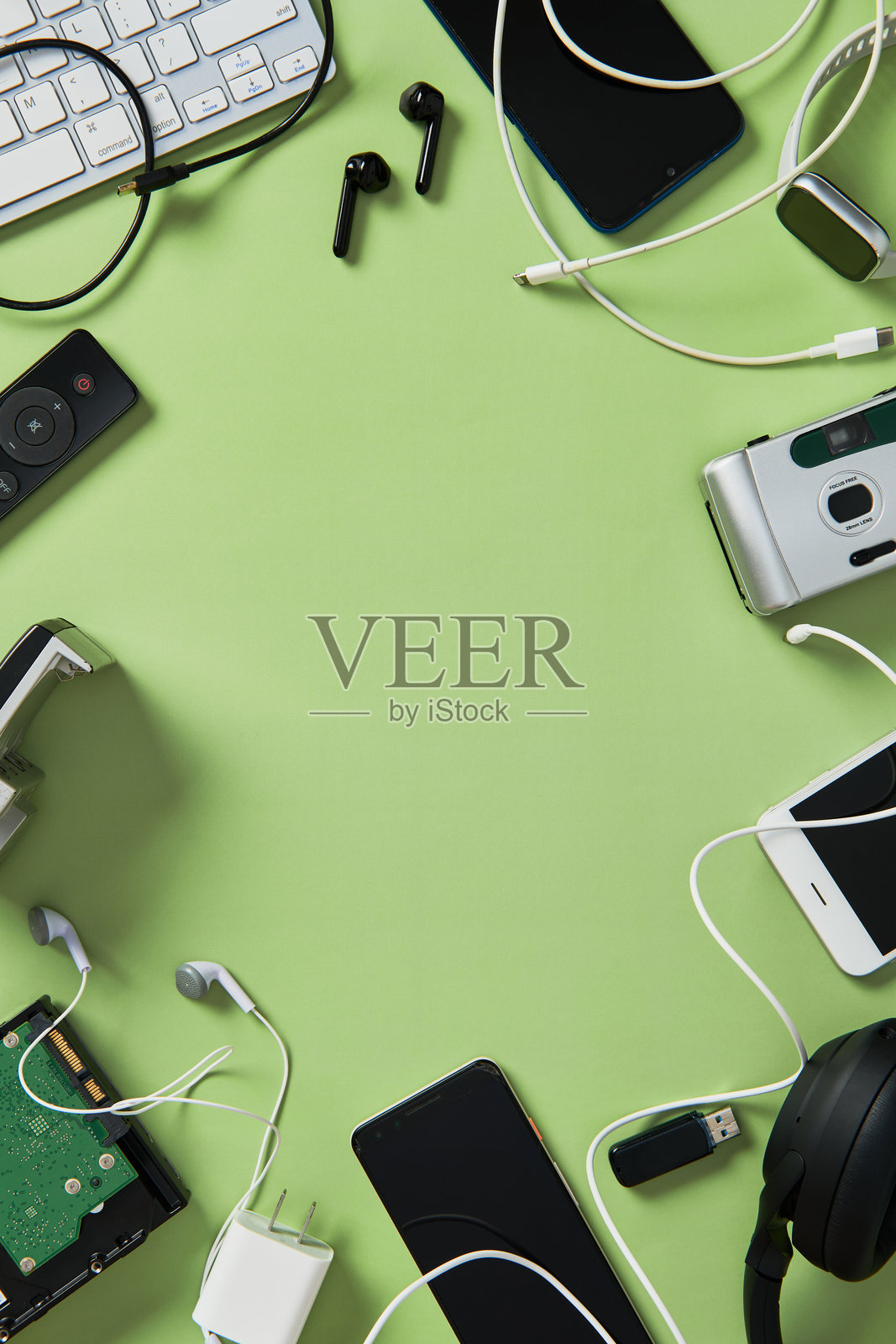 电子废弃设备和小工具的框架，如键盘、手机、相机、耳机，背景为绿色。俯视图，留有空白空间。照片摄影图片