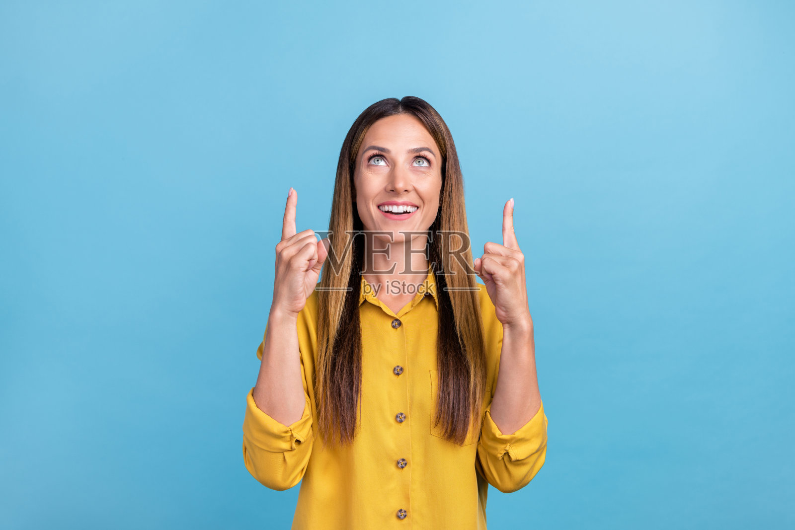 一位拥有漂亮棕色头发的千禧女性，穿着黄色衬衫，仰望着蓝色背景。照片摄影图片