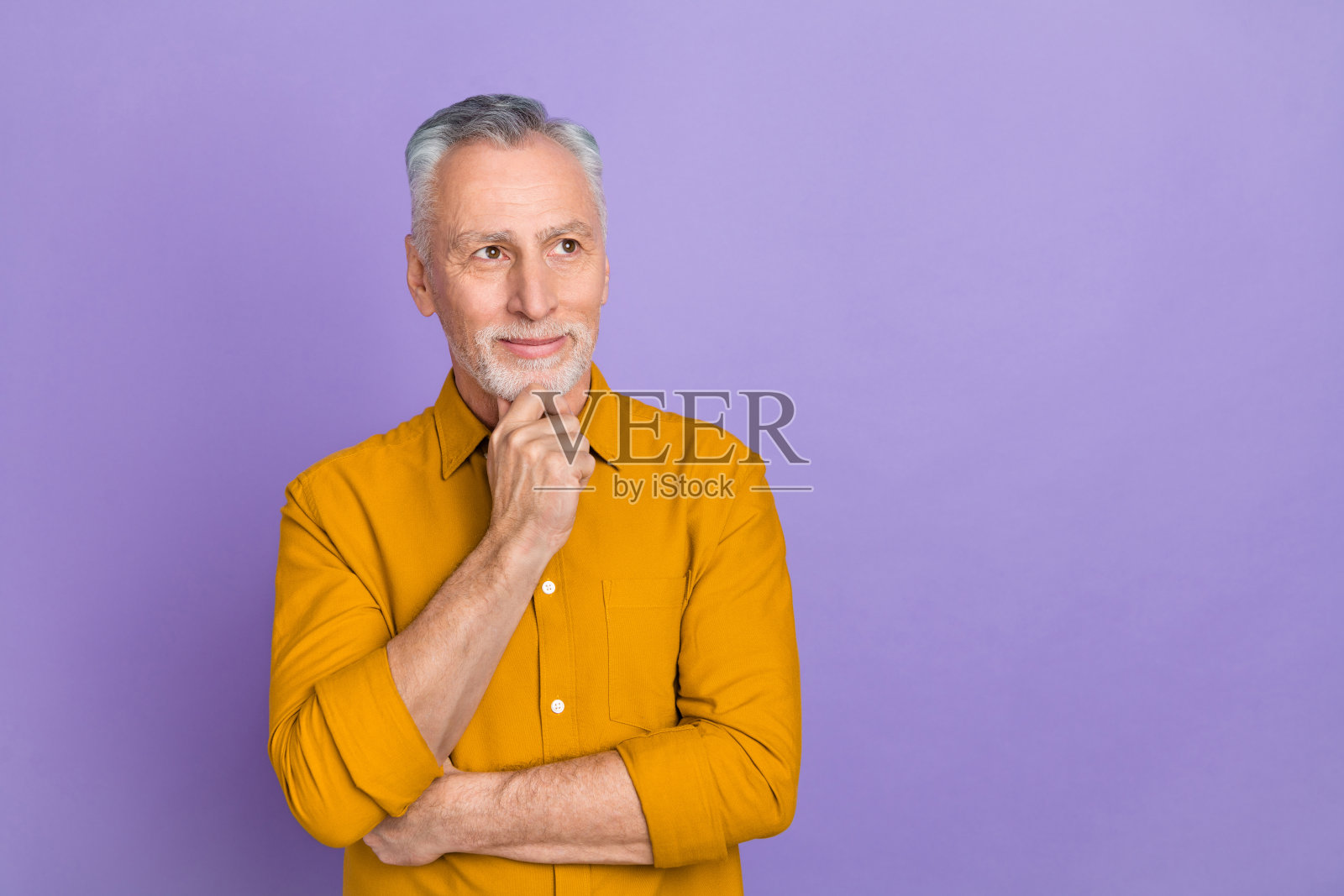 穿着黄色衬衫的优雅银发男士，双手托着脸，背景为紫色。照片摄影图片
