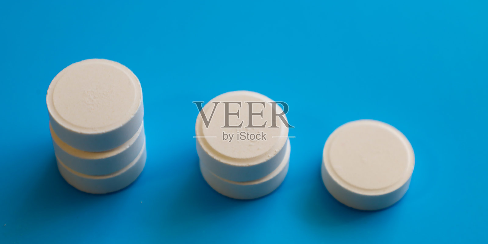 三堆不同高度的白色圆形药片排列在明亮的蓝色背景上。医学图像展示了剂量减少或治疗阶段。照片摄影图片