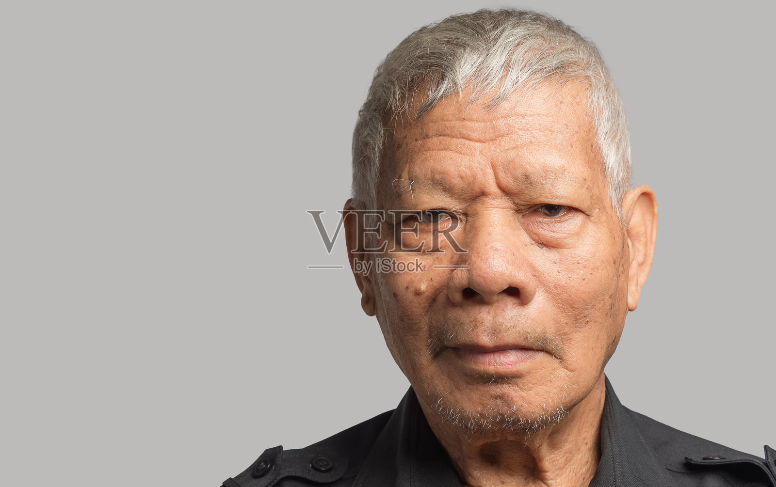 一位穿着衬衫的老年亚洲男子微笑着看向镜头，站在灰色背景前。照片摄影图片