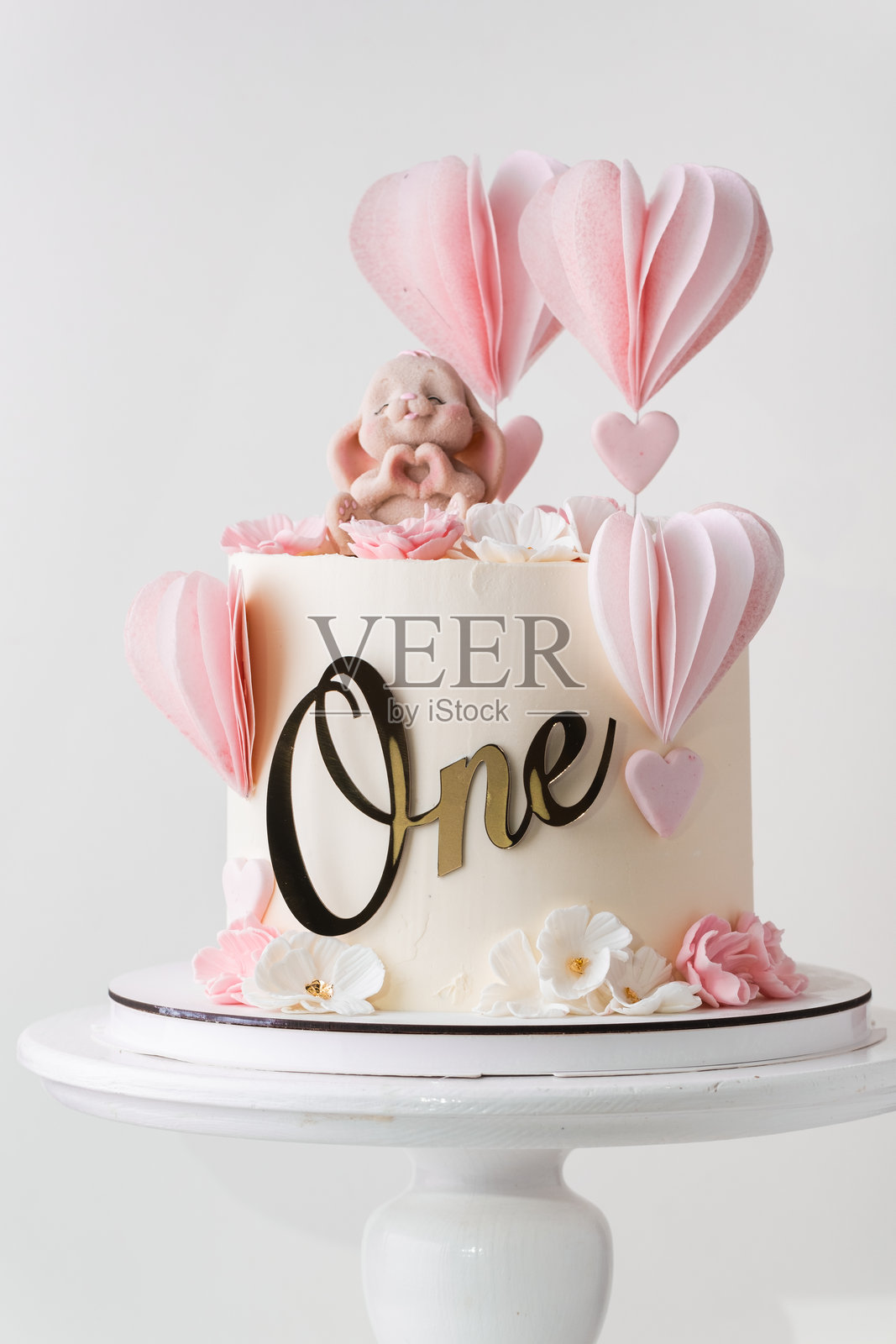 漂亮的粉色生日蛋糕，适合一岁的小女孩，上面装饰着巧克力小兔子雕像。白色背景。照片摄影图片