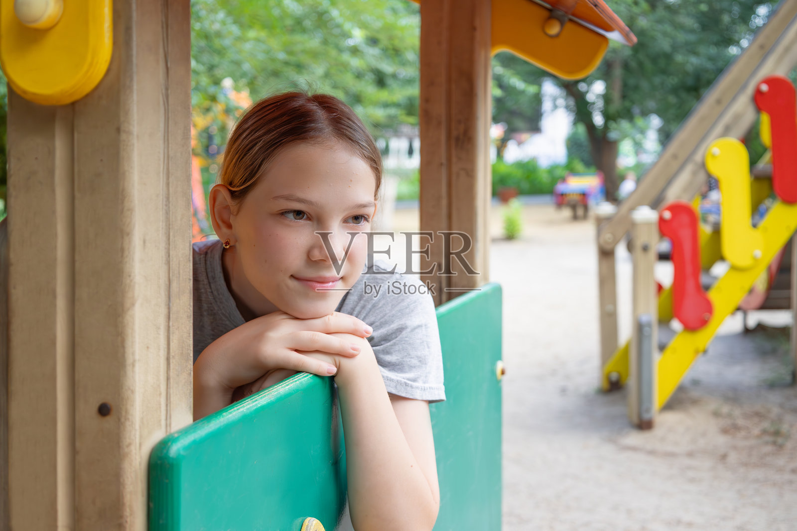 微笑的女孩靠在游乐场玩具屋的窗户上，享受夏日的美好时光照片摄影图片