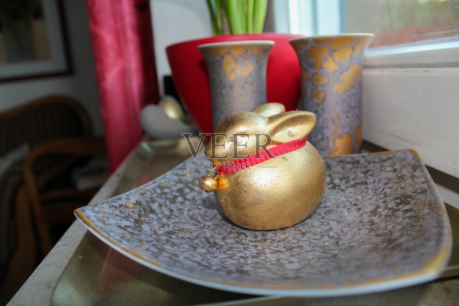 金色兔子与铃铛在陶瓷盘上 – 温馨室内环境中的优雅复活节装饰照片摄影图片