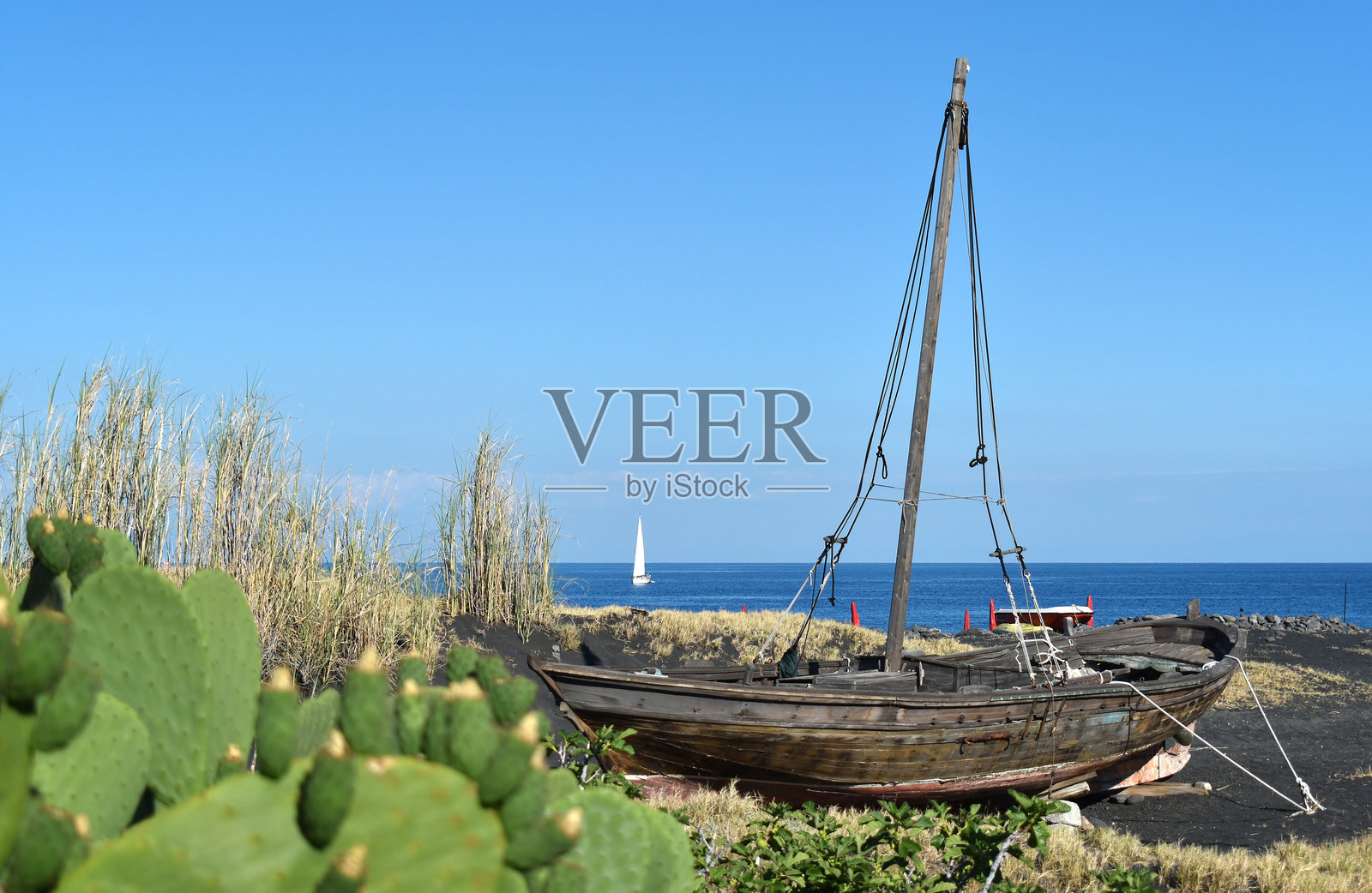 一艘船停靠在斯特龙博利岛的黑色火山沙滩上，背景中海面上有一艘白色帆船，意大利西西里，欧洲照片摄影图片