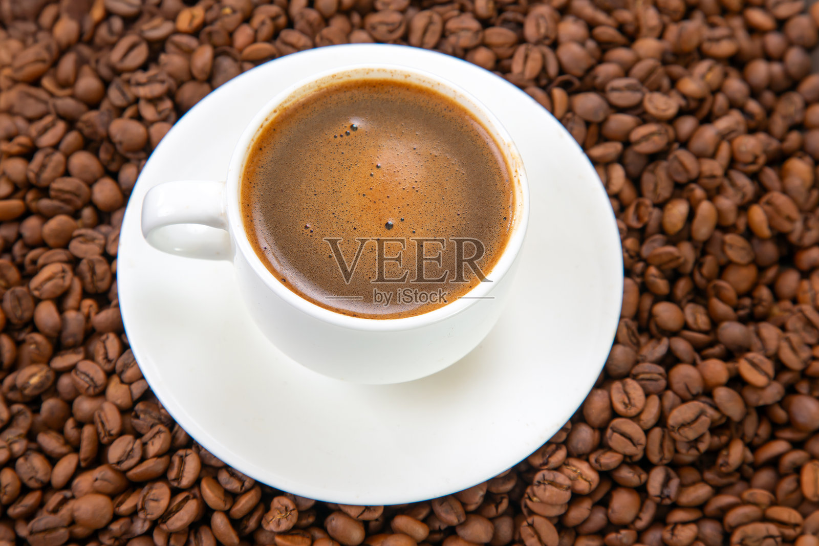 浓郁的深色浓缩咖啡，顶部有泡沫奶油，盛在白色陶瓷杯中，优雅地放置在碟子上，周围散落着咖啡豆，营造出温馨宜人的咖啡场景照片摄影图片