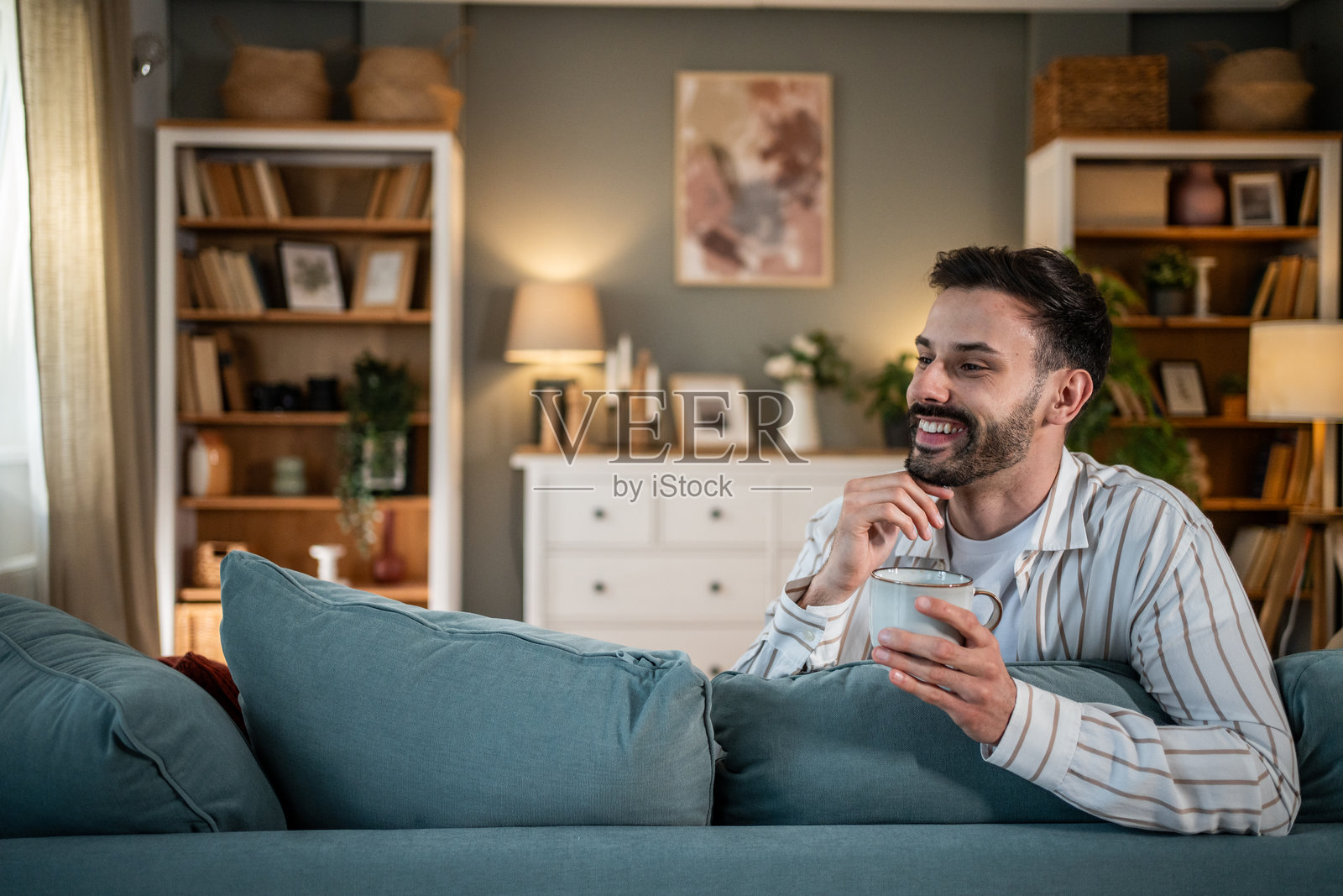 年轻男子在舒适的客厅沙发上放松，享受一杯咖啡照片摄影图片