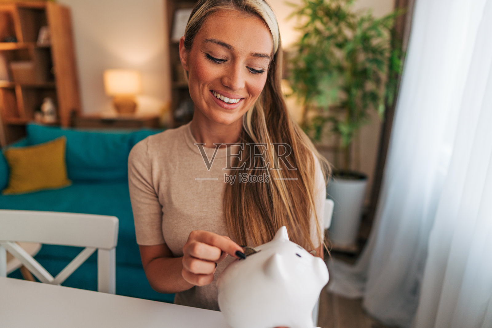 年轻女性在家中把钱存进储蓄罐照片摄影图片