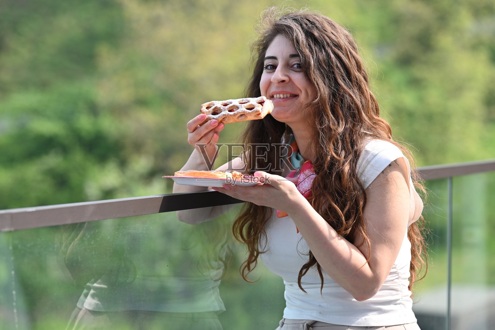 年轻女性在郁郁葱葱的夏季公园中享用新鲜的可颂面包照片摄影图片
