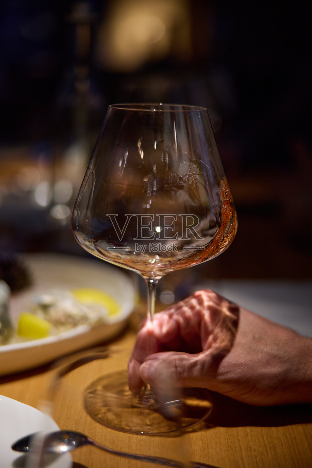 香槟品尝，酒杯摆放在桌上，时尚的桌面布置，一只手握着一只优雅的玫瑰色起泡酒杯，柔和的灯光，一盘生蚝和柠檬。照片摄影图片