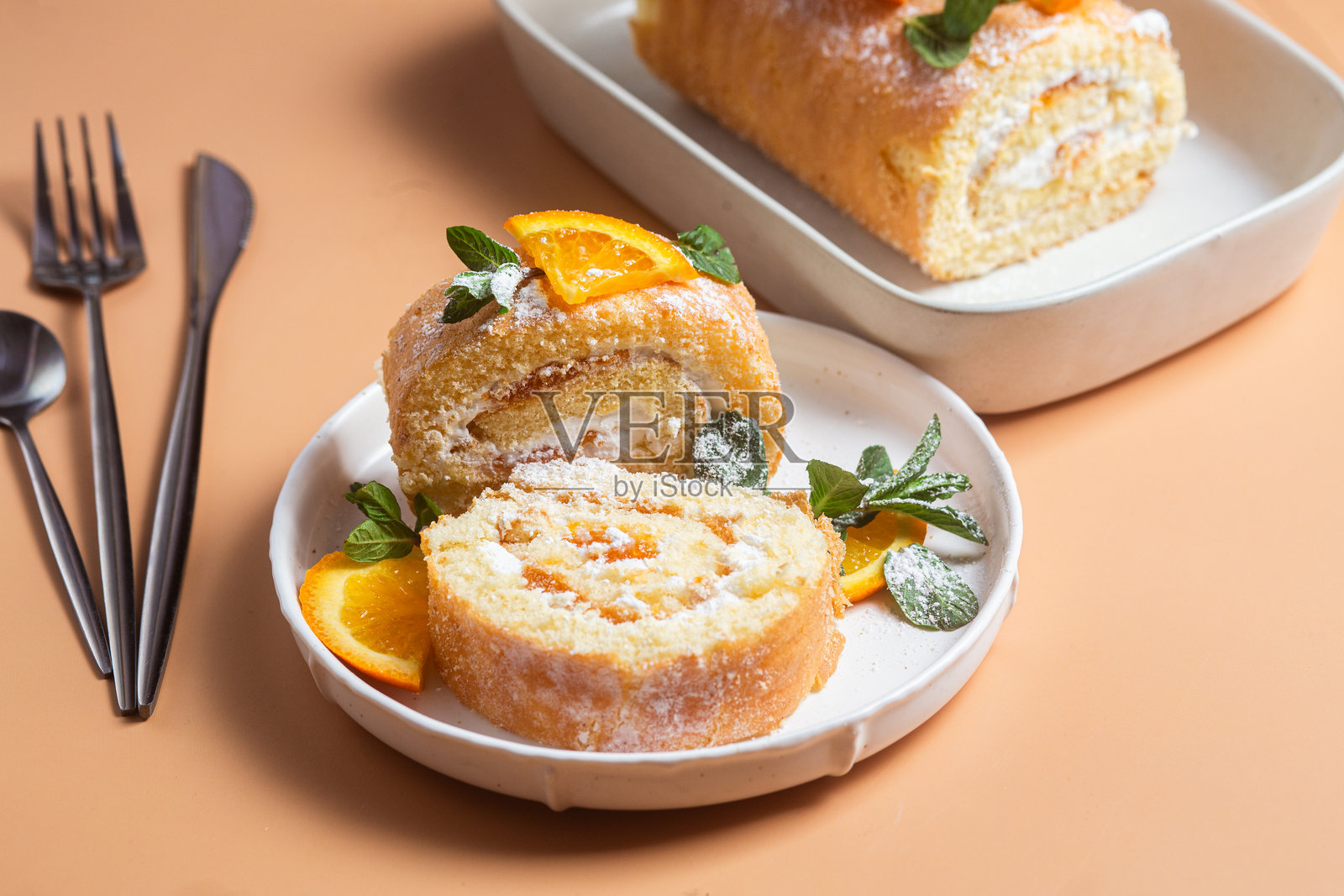 橙色海绵蛋糕卷上面夹着奶油和薄荷，放在明亮背景的白色盘子里照片摄影图片