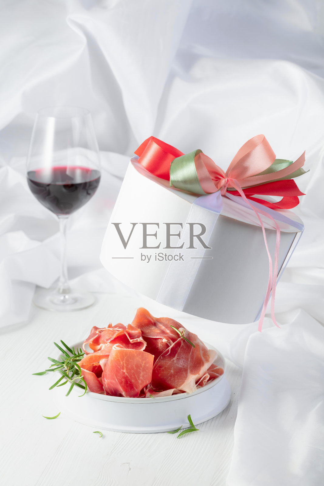 礼盒中的火腿与迷迭香，以及白色木桌上的一杯红酒。照片摄影图片