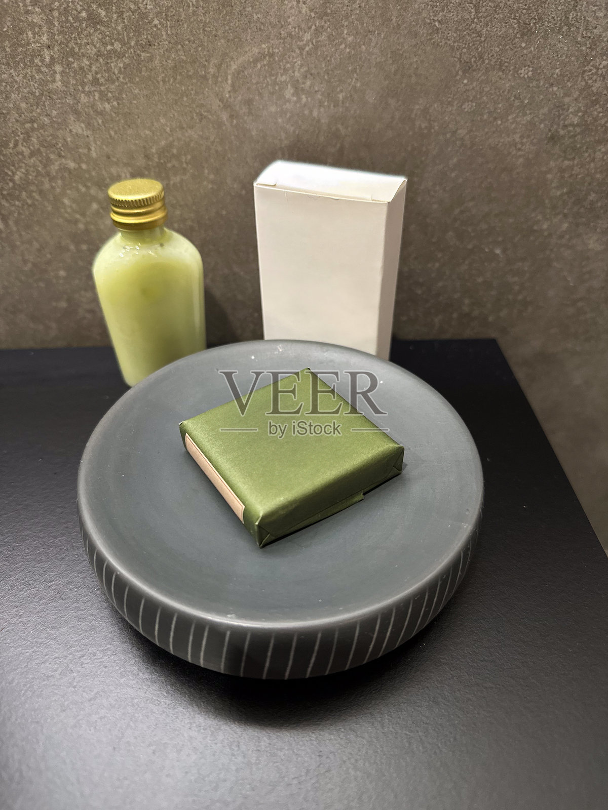 酒店浴室内陶瓷盘上的绿色包装香皂，旁边有洗漱用品。清洁、关怀、健康和旅行款待。照片摄影图片
